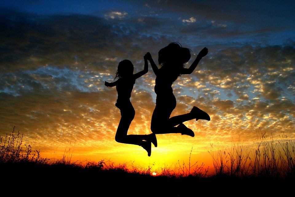 two females jumping holding hands infront of sunset