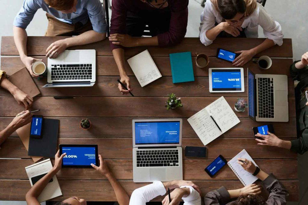 Team working around a large wooden table with laptops, tablets, and notebooks