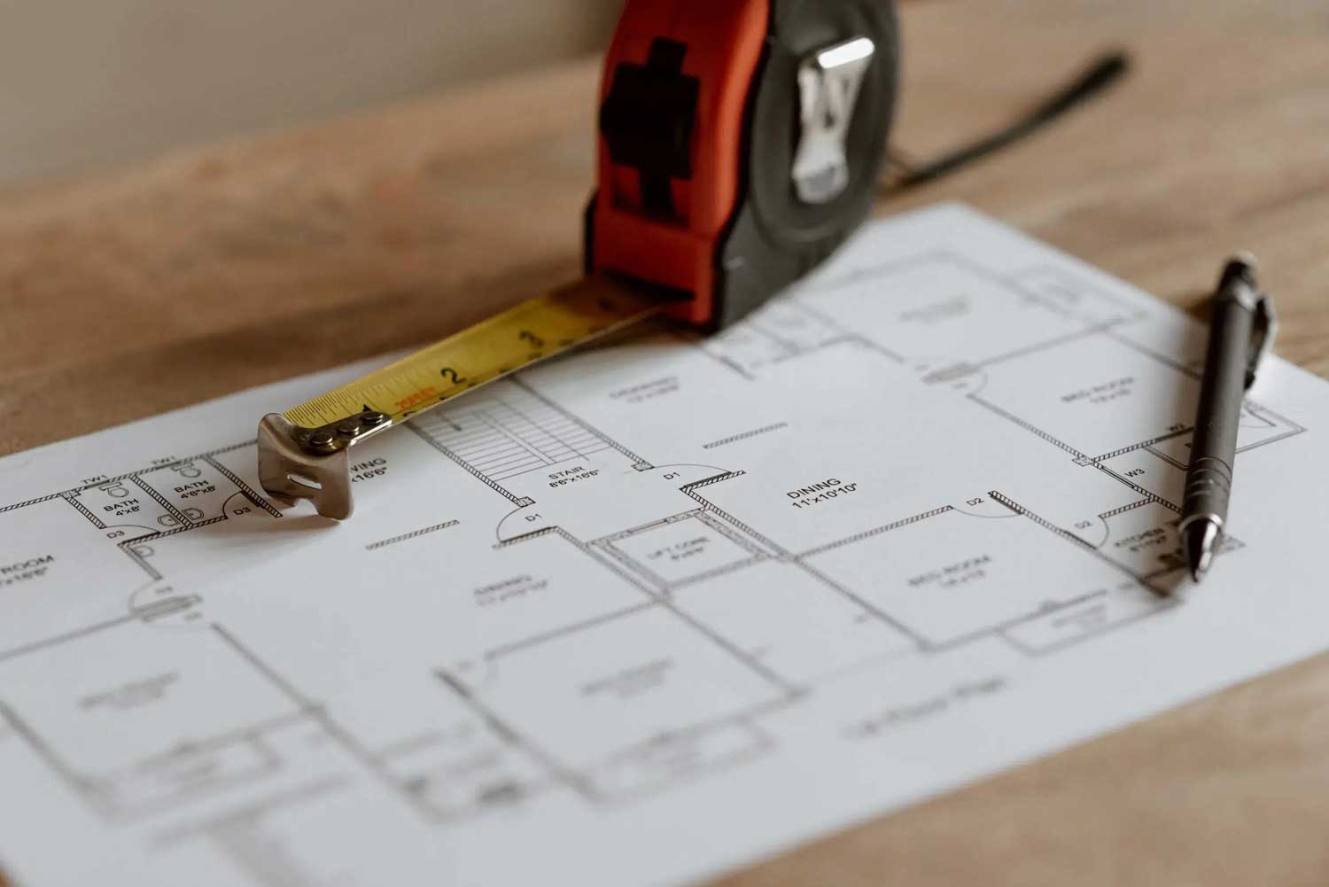 Architectural floor plan with a tape measure and pen on a wooden desk
