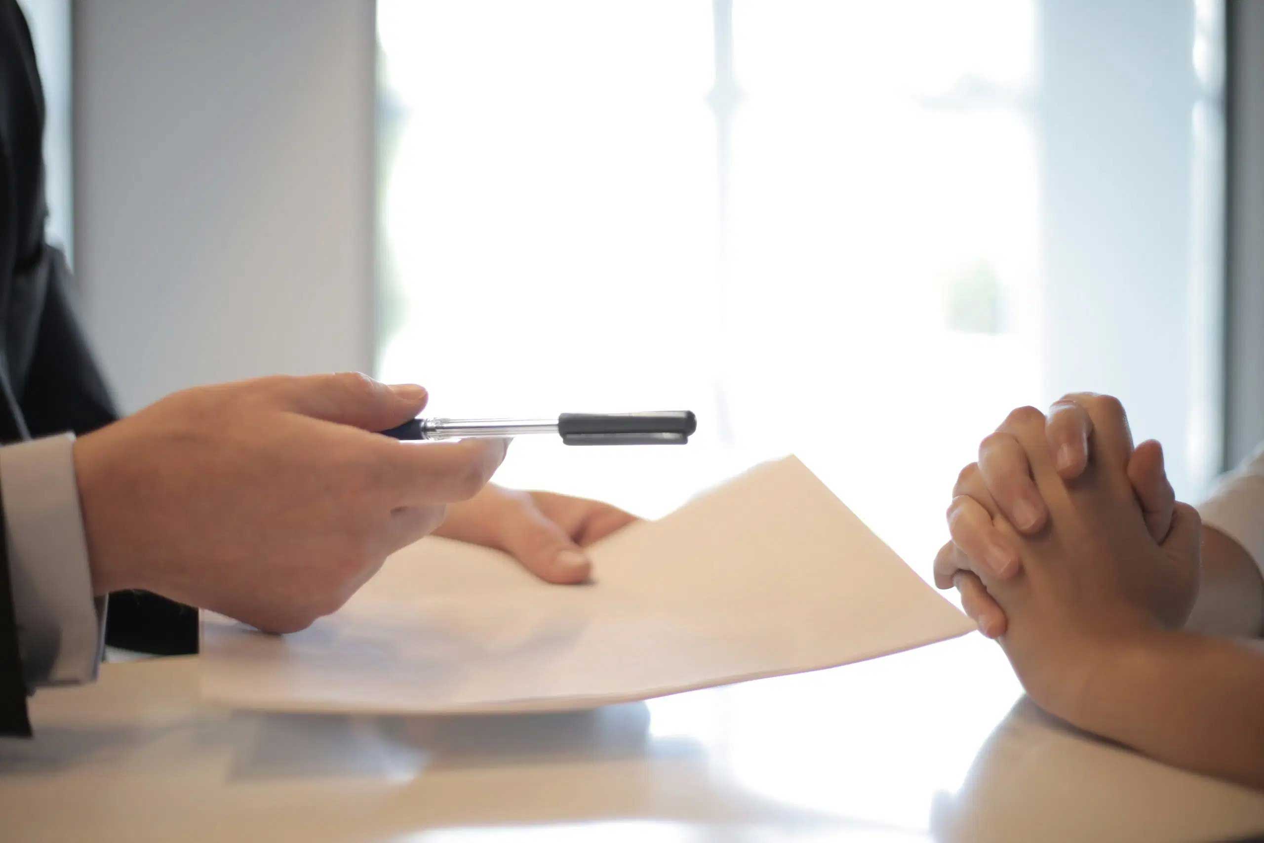 house-building-800x400 Person handing over a pen and contract paper across a table during a meeting