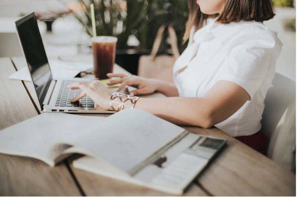 Woman working on a laptop at a wooden desk with coffee and documents