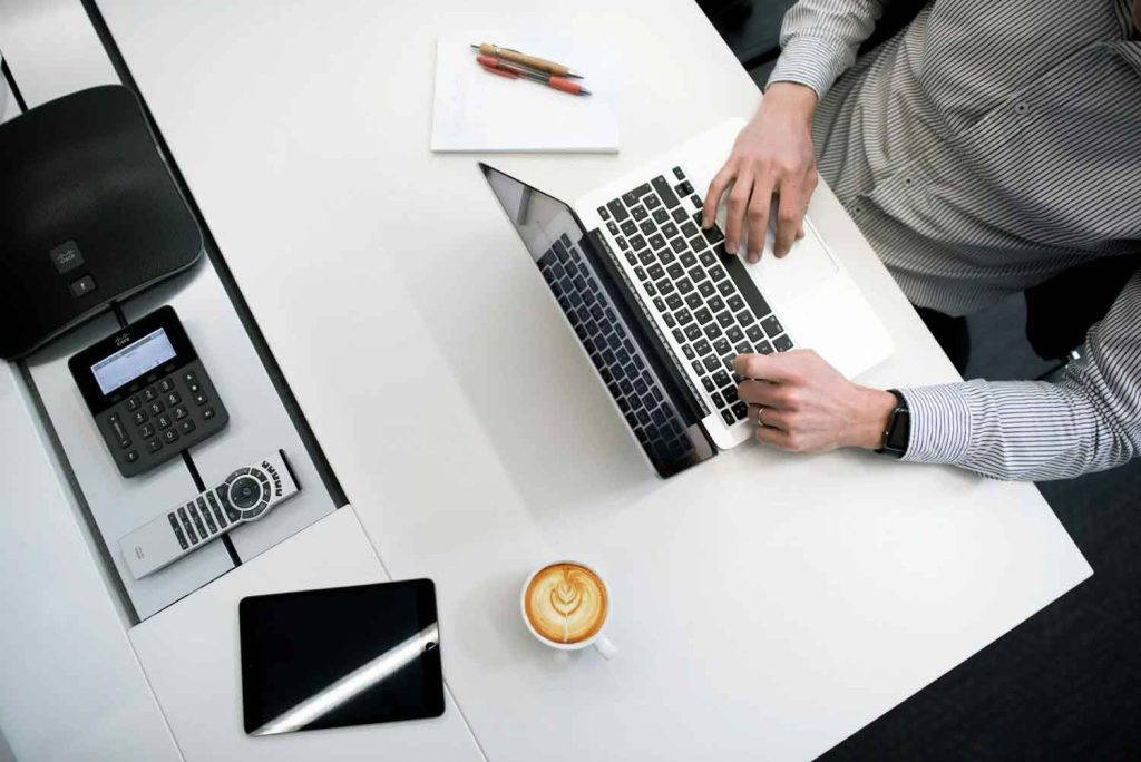 Top view of a person working on a laptop at a modern desk with coffee and office devices