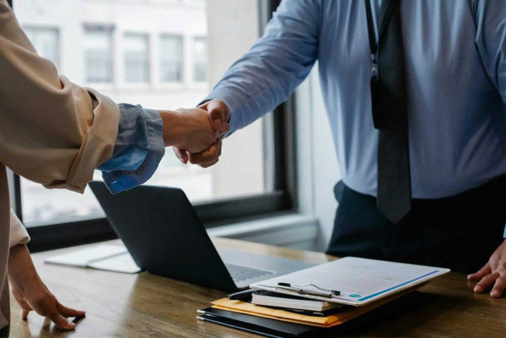 Two professionals shaking hands over a desk in an office setting